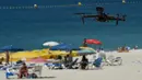 Sebuah drone atau pesawat tak berawak yang diterbangkan oleh polisi setempat memperingatkan orang-orang untuk menjaga jarak di pantai Areas di Sanxenxo, Spanyol, Selasa (14/7/2020). Drone tersebut untuk memantau jaga jarak antarwisatawan saat berlibur di masa pandemi Corona. (MIGUEL RIOPA / AFP)