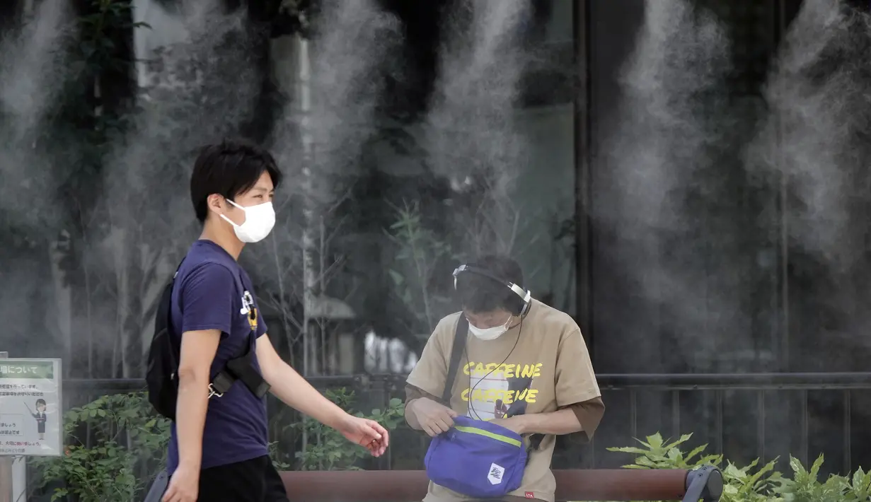 Para pria yang mengenakan masker wajah untuk membantu melindungi diri dari penyebaran virus corona melakukan pendinginan di titik kabut yang menyejukkan di Tokyo, Selasa (10/8/2021). (AP Photo/Eugene Hoshiko)