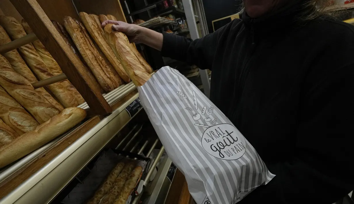 Pemilik toko roti Florence Poirier memasukkan baguette ke dalam kantong untuk pelanggan di toko roti, di Versailles, sebelah barat Paris, Selasa, 29 November 2022.  Baguette Prancis resmi diberi status warisan budaya takbenda UNESCO pada Rabu, 30 November 2022. (AP Photo/Michel Euler)