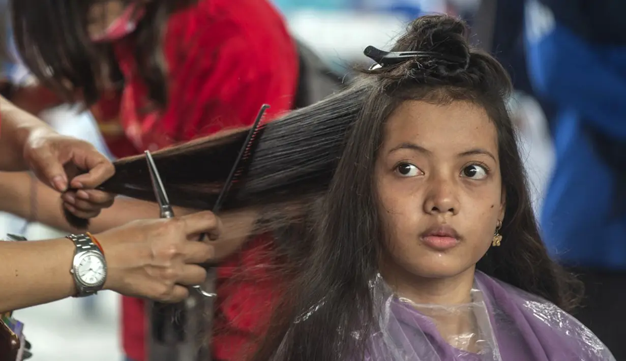 Seorang wanita mengikuti cukur rambut gratis saat acara amal di Surabaya, Jawa Timur, Senin (8/11/2021). Layanan cukur rambut gratis ini dilakukan kepada 100 anak yatim piatu. (Juni Kriswanto/AFP)