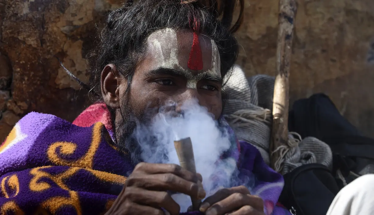 Seorang Sadhu atau orang suci Hindu menghisap ganja menjelang festival Hindu 'Maha Shivaratri', di Kathmandu (9/3/2021). Ratusan orang suci datang ke kuil untuk mengisap ganja, mereka dapat merokok ganja (hanya di kuil) dan melaburi tubuhnya dengan abu. (AFP/Prakash Mathema)