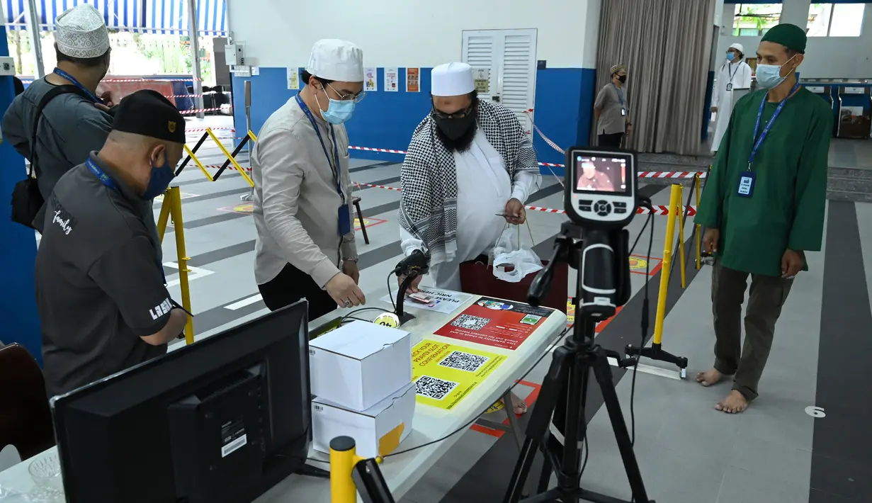 Umat muslim memindai identitas setibanya untuk salat Jumat usai pencabutan pembatasan Covid-19 di Masjid Al-Istighfar, Singapura, Jumat (26/6/2020). Masjid-masjid di Singapura menyediakan 2 sesi setiap Jumat dengan kuota yang diperbolehkan adalah 50 orang pada satu waktu. (Roslan RAHMAN/AFP)