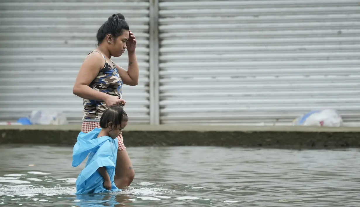 Seorang wanita dan seorang anak mengarungi jalan yang terendam banjir di kota Valenzuela, Filipina pada Rabu, 2 Agustus 2023. (AP Photo/Aaron Favila)