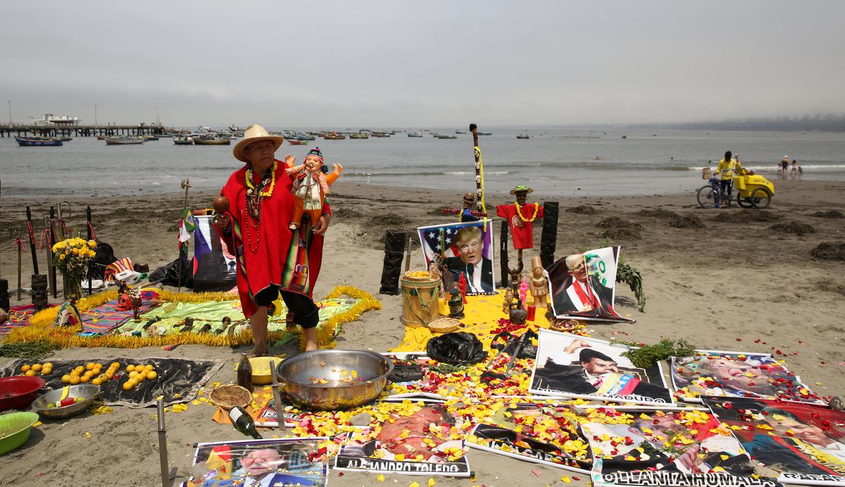 Seorang dukun menggelar ritual dengan meletakkan sejumlah poster bergambar para pemimpin dunia di Pantai Agua Dulce di Lima, Peru, (29/12). Para dukun ini meramalkan AS akan diselimuti dengan malapetaka dan kesuraman pada 2017. (Reuters/Mariana Bazo)