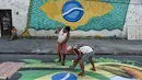 Pemandangan saat warga melukis mural Piala Dunia 2018 bergambar bendera Brasil di jalanan Camboata, Rio de Janeiro, Brasil, Kamis (31/6). (Fabio TEIXEIRA/AFP)