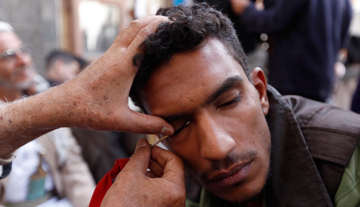 Seorang pria saat kelopak matanya dirias dengan kohl atau celak di  Masjid Agun di kota tua ibukota Sanaa, Yama, (19/5). Pemakaian kohl atau celak diyakini muslim Yaman mampu membersihkan dan melindungi mata dari penyakit. (AFP Photo/Mohammed Huvais)