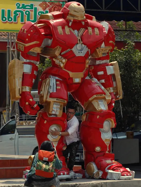 Seorang turis saat mengabadikan temannya yang sedang berpose di patung "Iron Man Robot" di kuil Tamru, Thailand, (3/3). Patung superhero seperti "Hulk", "Superman" dan "Iron Man" dipajang demi menarik pengunjung kuil. (REUTERS/Chaiwat Subprasom)