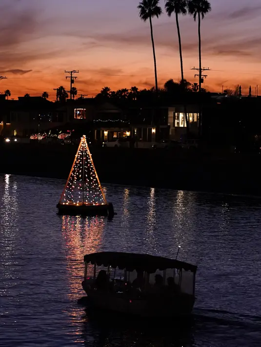 Perahu melewati lampu pohon Natal yang mengapung di Long Beach, California, Minggu (19/12/2021). Sambut Natal, pantai di California menghiasi pantainya dengan hiasan lampu pohon Natal. (AP Photo/Ashley Landis)