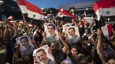 Pendukung mengibarkan bendera nasional dan foto Presiden Suriah Bashar Assad saat mereka merayakan kemenangannya di Omayyad Square, di Damaskus, Kamis (27/5/2021). Bashar al-Assad terpilih kembali untuk masa jabatan keempat sebagai presiden Suriah yang dilanda perang. (AP Photo/Hassan Ammar)