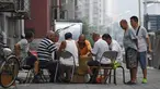 Sekelompok pria bermain kartu remi di trotoar di luar gedung apartemen di Beijing, China (10/8). Kartu remi, adalah sekumpulan kartu seukuran tangan yang digunakan untuk permainan kartu. (AFP Photo/Greg Baker)