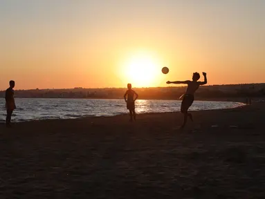 Sejumlah orang bermain bola saat matahari terbenam di pantai Sampieri, Sisilia, (31/7). (AFP Photo/Ludovic Marin)