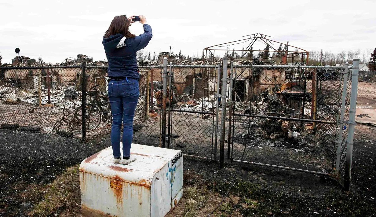 Seorang wanita mengambil foto sisa-sisa kebakaran hutan yang terjadi beberapa hari lalu di kAbasand, Fort McMurray, Alberta, Kanada, (9/5). Kebakaran ini menghanguskan 7.500 hektare lahan. (REUTERS/Chris Wattie)