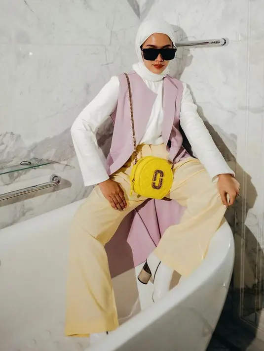 Influencer Ana Octarina mengenakan outer lilac yang dipadu dengan blouse dan hijab putih. Untuk bawahan, ia memilih soft yellow pants. (Instagram/anaoctarina).