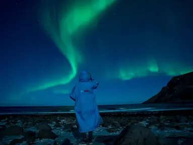 Seseorang menonton fenomena alam Aurora Borealis atau Northern Lights di Unstad, lingkaran Arktik, Norwegia, Sabtu (3/3). Aurora menampilkan banyak warna, tapi yang sering muncul adalah hijau muda dan pink. (Olivier MORIN/AFP)