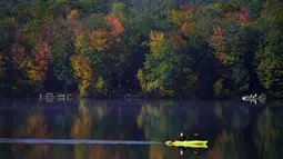 Virginia Davidson mendayung kayak di Moose Pond di mana pepohonan di sekitarnya berubah menjadi warna musim gugur, di Bridgton, Maine, Amerika Serikat, Rabu (13/10/2021). Salah satu yang paling khas dari musim gugur adalah pohon-pohon yang berubah warna sebelum gugur. (AP Photo/Robert F. Bukaty)