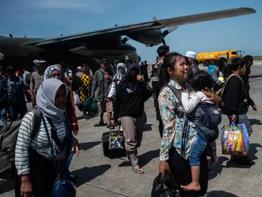 Seorang wanita membawa anaknya ketika mereka tiba di Surabaya, Kamis (4/10). Banyak anak-anak yang terpisah dari keluarganya setelah bencana gempa-tsunami melanda Palu dan Donggala pada 28 September. (AFP Photo/Juni Kriswanto)