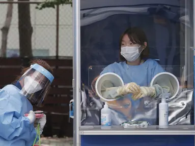 Seorang pekerja medis memegang kipas angin portabel selama panas terik sementara petugas polisi menjalani tes COVID-19 di klinik darurat di Badan Kepolisian Metropolitan Seoul di Seoul, Korea Selatan, Rabu, (19/8/2020). (AP Photo / Ahn Young -joon)