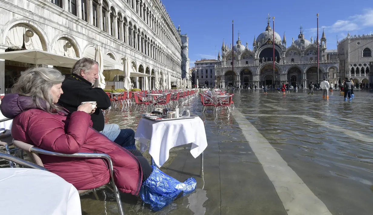 Orang-orang duduk di bar di St. Mark's Square yang terendam banjir di Venesia, Italia, Jumat (5/11/2021). Setelah Venesia mengalami banjir terparah kedua dalam sejarahnya pada November 2019, kota itu dibanjiri empat kali pasang luar biasa dalam waktu enam minggu. (AP Photo/Luigi Costantini)