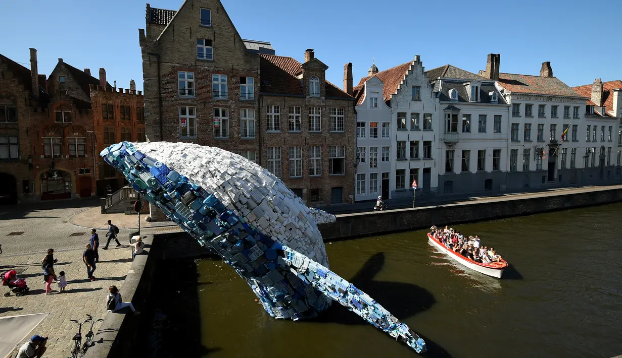 Sebuah perahu wisatawan berlayar melewati instalasi patung paus yang ditampilkan di sungai Brugges, Belgia, Sabtu (14/7). Patung paus berukuran 12 meter itu terbuat dari 5 ton sampah plastik yang mengambang di Samudra Pasifik dan Atlantik. (AFP/JOHN THYS)