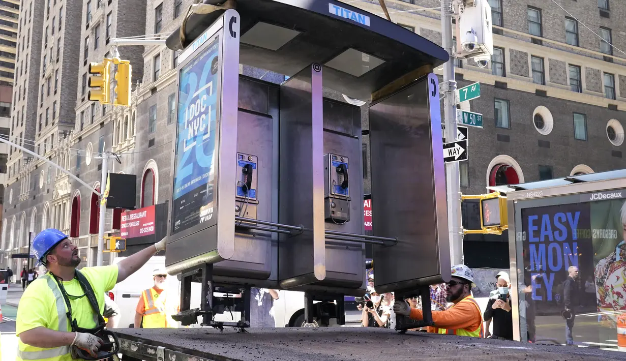 Para pekerja memindahkan bilik telepon umum terakhir NYC di dekat Seventh Avenue dan 50th Street di Midtown Manhattan, New York City, pada 23 Mei 2022. Bilik telepon itu adalah salah satu peninggalan terakhir dari lebih dari 8.000 telepon umum di seluruh kota yang telah disingkirkan satu per satu selama beberapa tahun terakhir. (TIMOTHY A. CLARY / AFP)