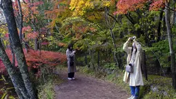 Orang-orang yang memakai masker untuk membantu mengekang penyebaran virus corona berfoto sambil berjalan di sepanjang jalan setapak saat pepohonan mulai berubah warna dedaunan musim gugur di Nagano, barat laut Tokyo, Jepang, Senin (26/10/2020). (AP Photo/Kiichiro Sato)
