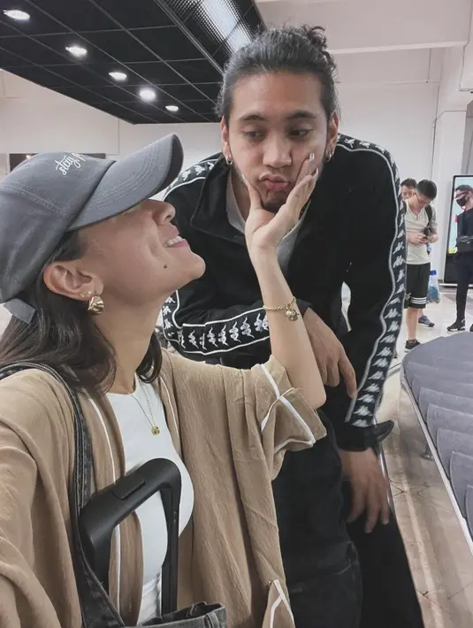 Sambil menunggu bagasi, Yasmin sempat memegang wajah kekasih. Mereka tak malu bermesraan di depan banyak orang