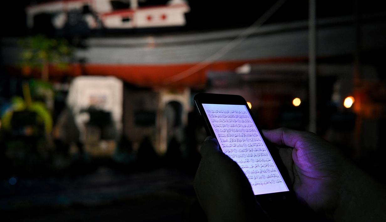 Seorang pria membaca Alquran di ponselnya saat upacara doa pada malam peringatan 17 tahun tsunami Boxing Day 2004 di monumen Kapal Tsunami Lampulo di Banda Aceh (25/12/2021). (AFP/Chaideer Mahyuddin)