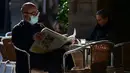 Seorang pria membaca koran di sebuah restoran di Barcelona, Spanyol, 23 November 2020. Restoran dan bar di Barcelona serta sekitar Catalonia kembali dibuka setelah tutup selama 40 hari untuk membendung peningkatan kasus virus corona COVID-19. (LLUIS GENE/AFP)