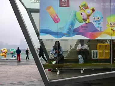 Orang-orang duduk di dalam stan yang dihiasi dengan poster Asian Games 2022 di sepanjang jalur pejalan kaki di sungai Qiantang di Hangzhou, provinsi Zhejiang, China pada 22 September 2023. (MANAN VATSYAYANA/AFP)