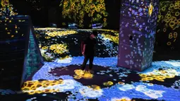 Seorang anggota staf berjalan melalui instalasi digital interaktif bernama "Shifting Valley, Living Creatures of Flowers, Symbiotic Lives" selama pratinjau media "teamLab Forest" di gedung hiburan BOSS E・ZO FUKUOKA di Fukuoka, Jepang, Jumat (16/7/2021). (YUKI IWAMURA/AFP)