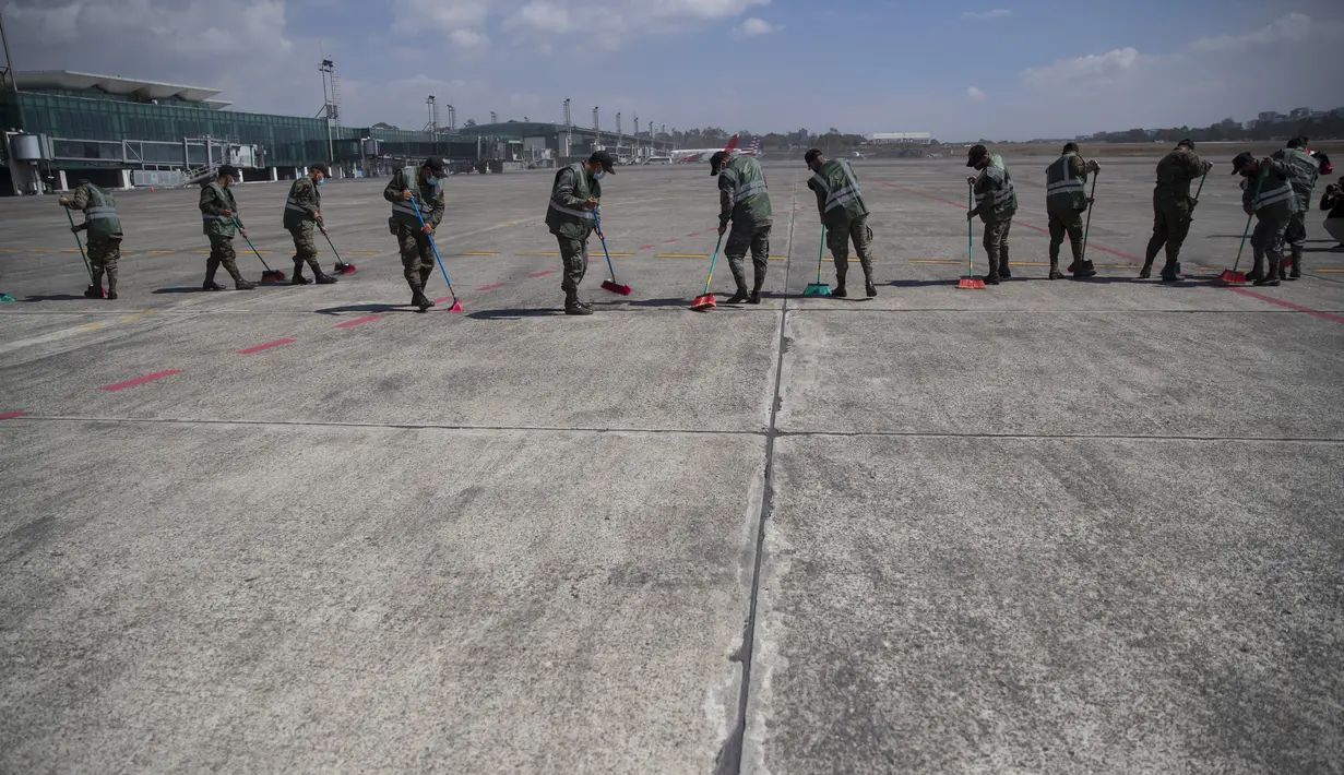 Tentara menyapu abu vulkanik dari landasan pacu di bandara Internasional La Aurora, yang telah ditutup akibat letusan di gunung berapi Pacaya di Guatemala City (23/3/2021). (AP Photo / Moises Castillo )