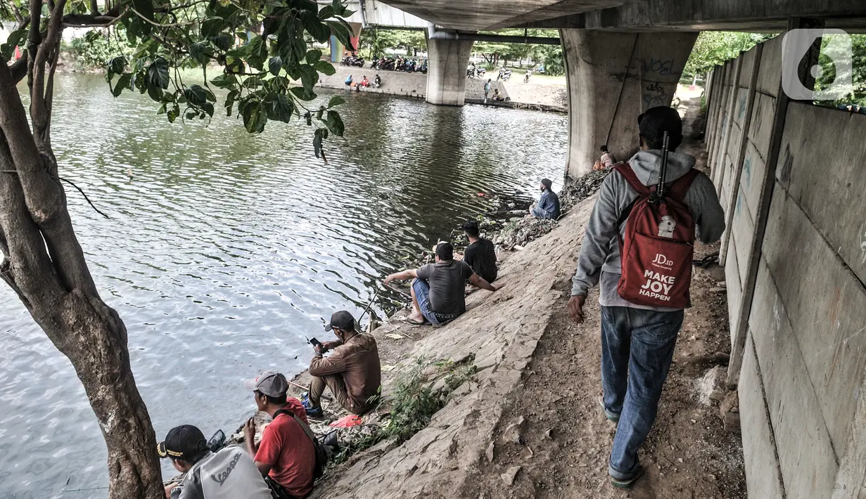 Seorang pria melewati warga yang memancing di waduk kawasan Sungai Bambu, Tanjung Priok, Jakarta, Minggu (17/1/2021). Waduk buatan di bawah Jalan Tol Pelabuhan tersebut menjadi wisata alternatif menghabiskan akhir pekan tanpa mengeluarkan biaya atau gratis. (merdeka.com/Iqbal S. Nugroho)