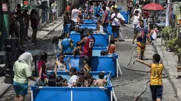 Anak-anak didampingi orang tua bermain di kolam portabel yang diberikan oleh pemerintah setempat untuk mendinginkan tubuh pada saat musim panas di Manila, Filipina (12/4). (AFP Photo/Noel Celis)