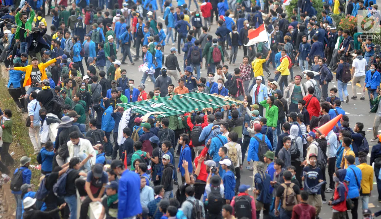 Mahasiswa menggotong pagar besi saat berdemonstrasi menolak pengesahan RUU KUHP dan revisi UU KPK di depan Gedung DPR, Jakarta, Selasa (24/9/2019). Demonstrasi berujung ricuh saat mahasiswa berusaha masuk ke area Gedung DPR. (merdeka.com/Arie Basuki)