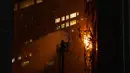Seorang petugas pemadam kebakaran menyemprotkan air ke api di Hong Kong, Jumat (3/3/2023). Petugas pemadam kebakaran Hong Kong sedang memadamkan kobaran api yang terjadi di lokasi konstruksi di distrik perbelanjaan populer kota itu. (AP Photo/Louise Delmotte)