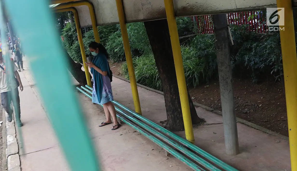 Seorang wanita menunggu di Halte Perum Tanjung Mas, Jakarta, Rabu (6/2). Proyek peninggian trotoar yang tidak diimbangi dengan renovasi halte menyebabkan bangku di halte menjadi pendek dan tidak layak untuk digunakan. (Liputan6.com/Immanuel Antonius)