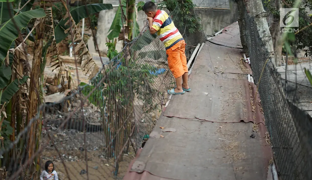 Seorang anak melihat ke bawah jembatan gantung semi permanen di Srengseng Sawah, Jakarta Selatan, Sabtu (24/8/2019). Warga terpaksa memanfaatkan jembatan tersebut untuk menyeberangi Sungai Ciliwung kendati kondisinya memprihatinkan dan berisiko menyebabkan kecelakaan. (Liputan6.com/ImmanuelAntonius)