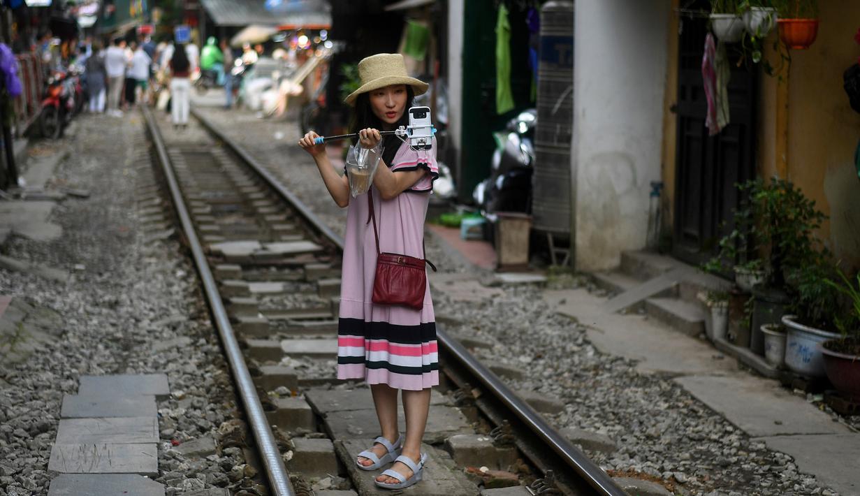 Foto pada 8 Juni 2019 memperlihatkan seorang wanita berswafoto di tengah jalur kereta api populer di Hanoi, Vietnam. Turis sengaja datang ke Old Quarter untuk berfoto di rel kereta api yang dianggap ' instagramable' tersebut. (Photo by Manan VATSYAYANA / AFP)
