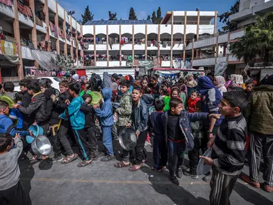 Anak-anak Palestina yang mengungsi berkumpul untuk menerima makanan di sebuah sekolah pemerintah di Rafah, Jalur Gaza selatan pada 19 Februari 2024. (MOHAMMED ABED/AFP)