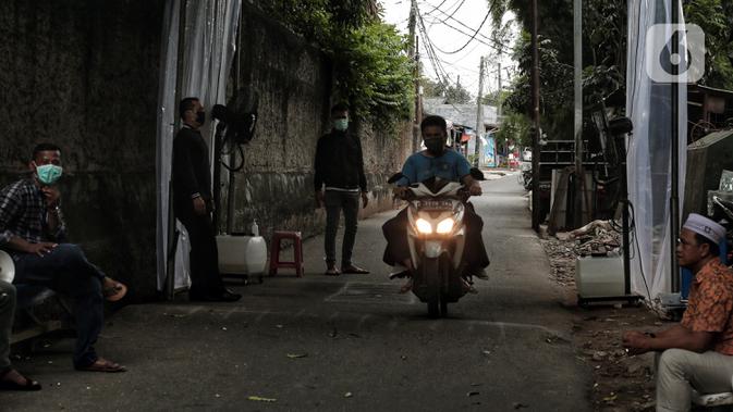 Pengendara sepeda motor melintasi tempat penyemprotan cairan disinfektan saat akan memasuki pemukiman warga di kawasan H. Gari, Pesanggrahan, Jakarta, Jumat (3/4/2020). Penyemprotan secara swadaya tersebut dilakukan warga untuk mencegah penyebaran virus corona COVID-19. (Liputan6.com/Johan Tallo)