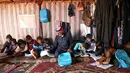 Abderrazaq Khatoun membantu tugas sekolah 11 cucunya di dalam tenda di desa Harbanoush, Suriah, 11 Maret 2021. Mengungsi dari rumah asalnya di provinsi Hama, Khatoun dan 30 anggota keluarga yang masih hidup mendirikan empat tenda di sebidang tanah yang dikelilingi pohon zaitun. (Ahmad al-ATRASH/AFP)