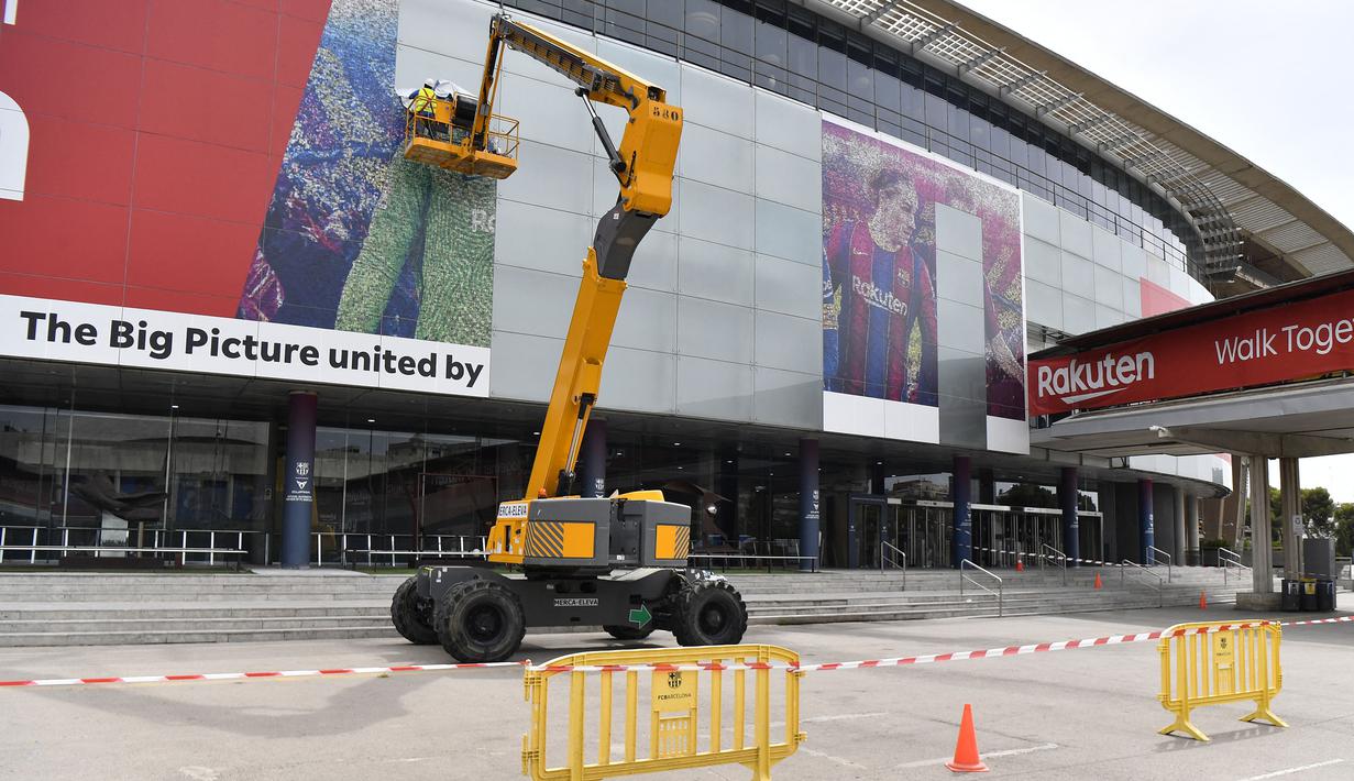 Pekerja melepas poster yang menampilkan pemain depan Argentina, Lionel Messi di pintu masuk Stadion Camp Nou, Barcelona pada Selasa, 10 Agustus 2021. Lionel Messi resmi meninggalkan Barcelona akibat masalah finansial klub dan peraturan dari Liga Spanyol. (AFP/Pau Barrena)