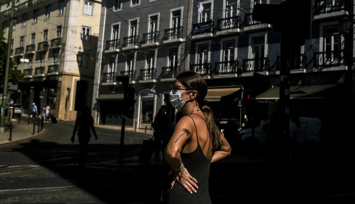 Seorang wanita yang mengenakan masker berdiri di depan alun-alun Camoes di Lisbon (14/7/2021). Hampir setengah dari populasi Portugal diberlakukan jam malam lagi awal bulan ini. (AFP/Patricia De Melo Moreira)