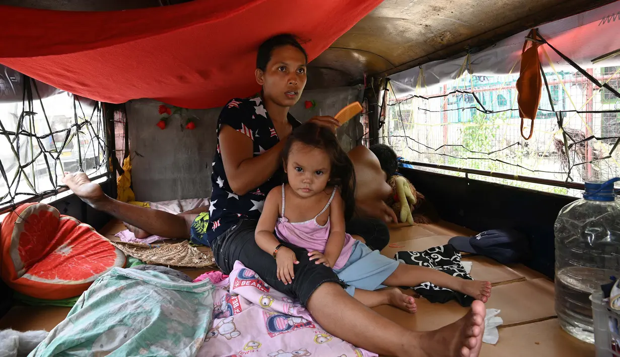 Istri pengemudi dan anaknya berada di dalam jeepney mereka yang berfungsi sebagai rumah sementara di Manila, 12 Agustus 2020. Angkutan ikonik di Filipina itu belum dapat mengangkut penumpang sejak Maret akibat lockdown Covid-19 yang membuat jutaan orang kehilangan pekerjaan. (Ted ALJIBE/AFP)