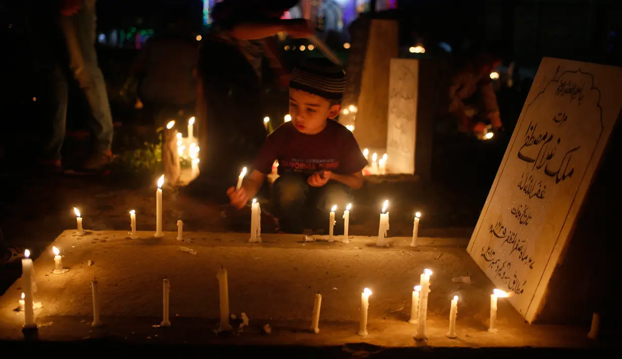 Seorang bocah memegang lilin di pemakaman keluarga dan saudara mereka saat memperingati Shab-e-Barat di pinggiran Srinagar, Kashmir (1/5). (AP Photo / Mukhtar Khan)