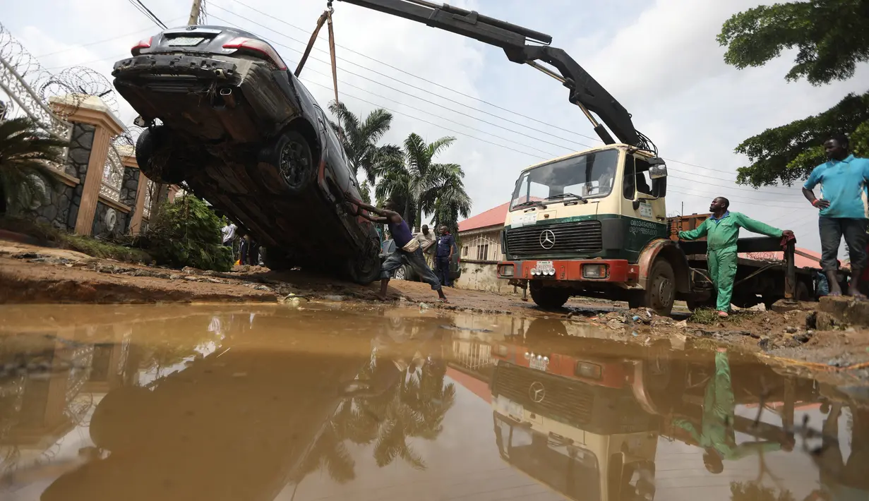 Orang-orang berusaha mengeluarkan mobil yang hanyut oleh air banjir di jalan yang terkena banjir bandang setelah hujan deras di Trademoore Estate, Lugbe, Abuja, Nigeria (13/9/2021). (AFP/Kola Sulaimon)