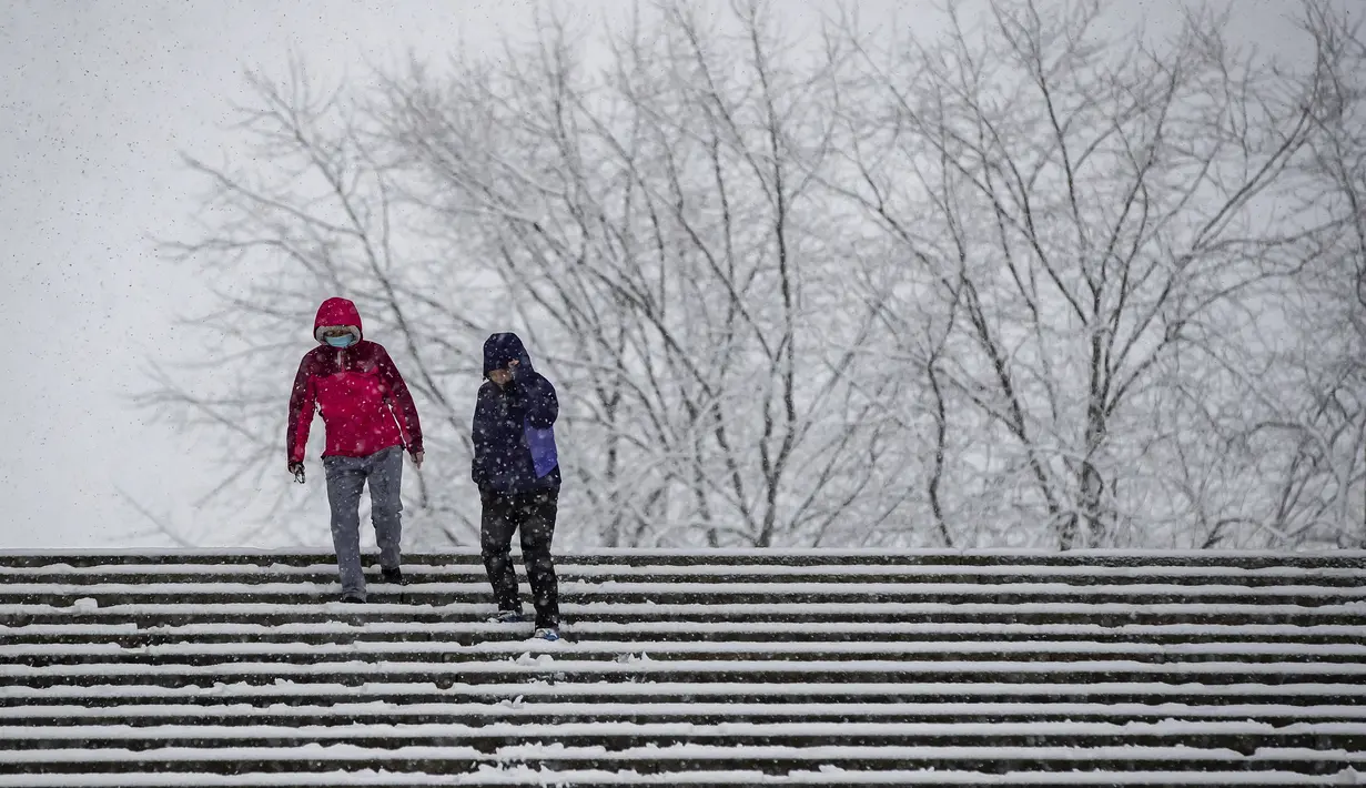 Warga mengenakan masker menuruni tangga yang dipenuhi salju di Universitas Simon Fraser, Burnaby, British Columbia, Kanada (21/12/2020). Salju lebat turun di beberapa bagian Burnaby terutama di dataran yang lebih tinggi seperti Gunung Burnaby dan Capitol Hill. (Darryl Dyck/The Canadian Press via AP)