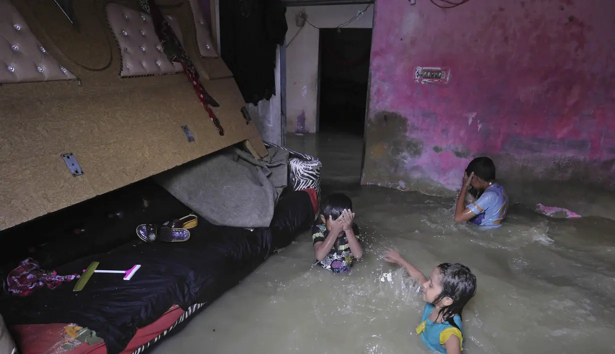 Anak-anak berdiri di kamar yang banjir di rumah mereka setelah hujan lebat di Karachi, Pakistan, Minggu, (26/7/2020). Tingginya banjir membuat air masuk ke rumah warga. (AP Photo/Fareed Khan)