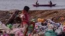 Seorang anak perempuan membawa adiknya berjalan di tumpukan sampah di permukiman kumuh di sepanjang garis pantai Pantai Baseco di Manila (28/9/2019). Daerah memiliki pantai yang sering dikunjungi beberapa warga Manila meskipun tingkat coliform berbahaya di perairan yang berdekatan. (AFP Photo/Maria