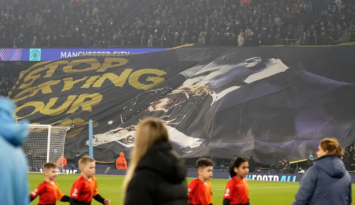 Suporter Manchester City membentangkan spanduk bergambar Rodri yang sedang mencium trofi penghargaan Ballon d'Or dan bertuliskan 'Stop Crying Your Heart Out' dalam laga leg 1 babak playoff Liga Champions 2024/2025 melawan Real Madrid di Etihad Stadium, Manchester, Inggris, Rabu (12/02/2025) WIB. (AP Photo/Dave Thompson)